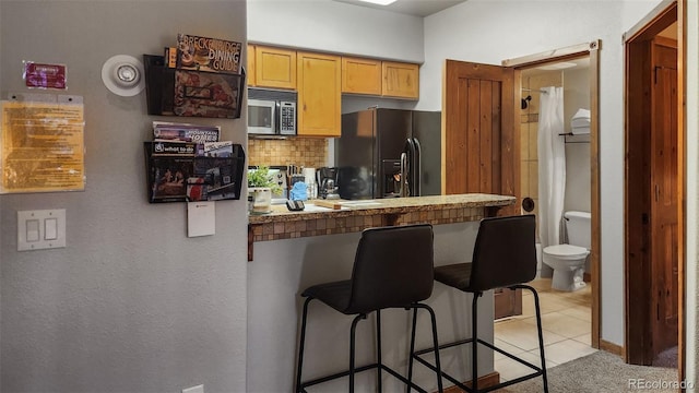 kitchen featuring a breakfast bar area, black fridge, light tile patterned floors, kitchen peninsula, and backsplash