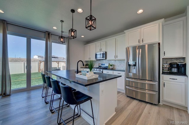 kitchen featuring dark countertops, a sink, appliances with stainless steel finishes, light wood-style floors, and a kitchen island with sink