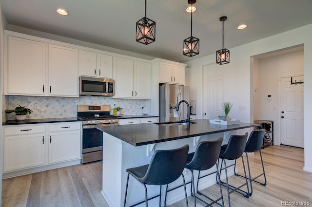 kitchen with light wood finished floors, a sink, appliances with stainless steel finishes, white cabinets, and a kitchen island with sink