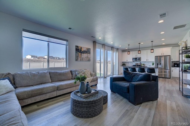 living area featuring light wood finished floors, visible vents, recessed lighting, and a textured ceiling