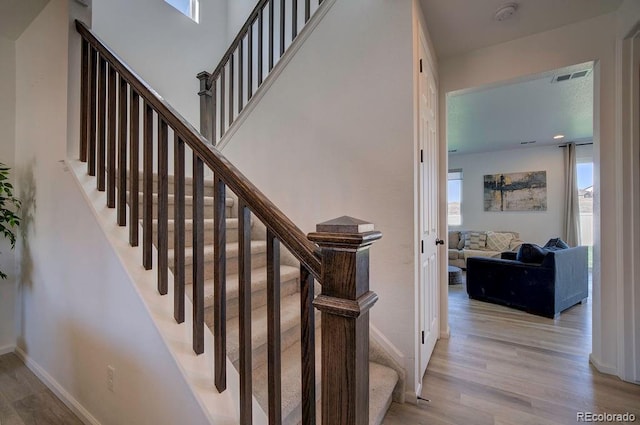 stairway with visible vents, a high ceiling, baseboards, and wood finished floors