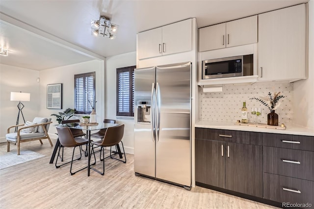 kitchen featuring white cabinetry, dark brown cabinets, stainless steel appliances, light hardwood / wood-style floors, and backsplash