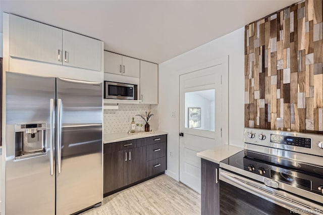 kitchen with tasteful backsplash, white cabinets, stainless steel appliances, dark brown cabinets, and light hardwood / wood-style flooring