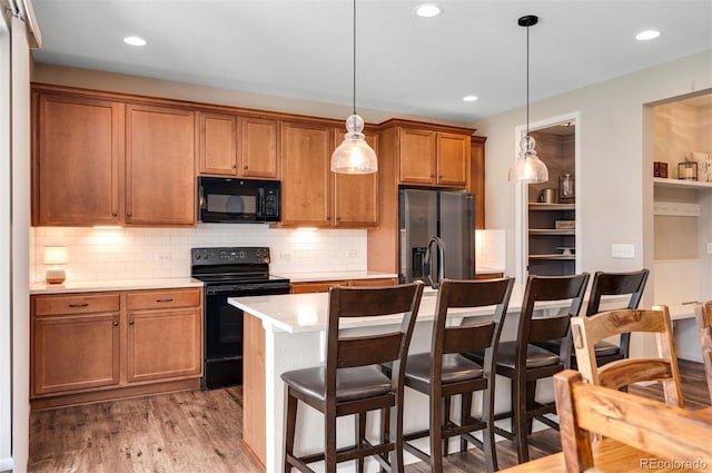 kitchen featuring light countertops, a breakfast bar area, brown cabinetry, and black appliances