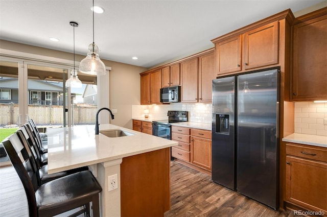 kitchen with a sink, brown cabinetry, dark wood-style flooring, black appliances, and decorative backsplash