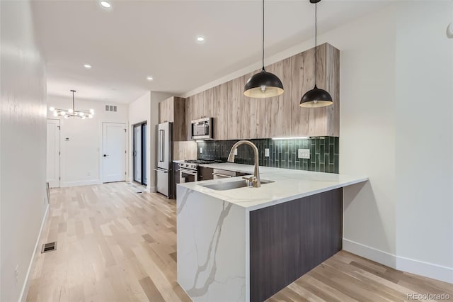 kitchen with sink, decorative light fixtures, kitchen peninsula, and premium appliances