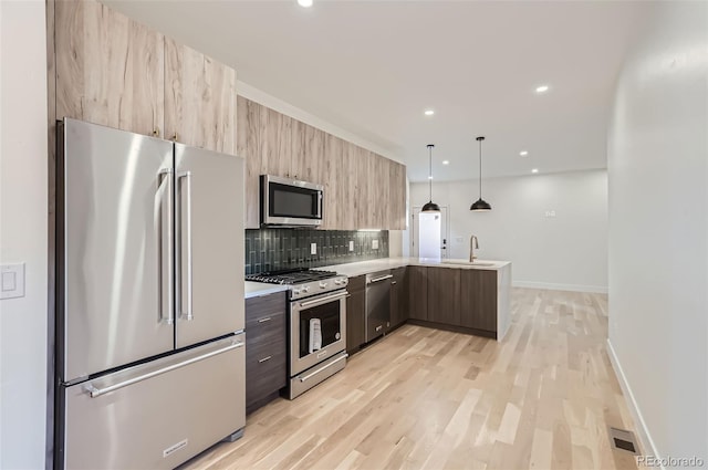 kitchen featuring kitchen peninsula, hanging light fixtures, stainless steel appliances, tasteful backsplash, and sink