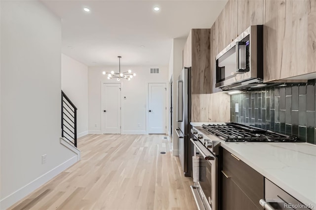 kitchen with light stone countertops, high end appliances, hanging light fixtures, a notable chandelier, and decorative backsplash