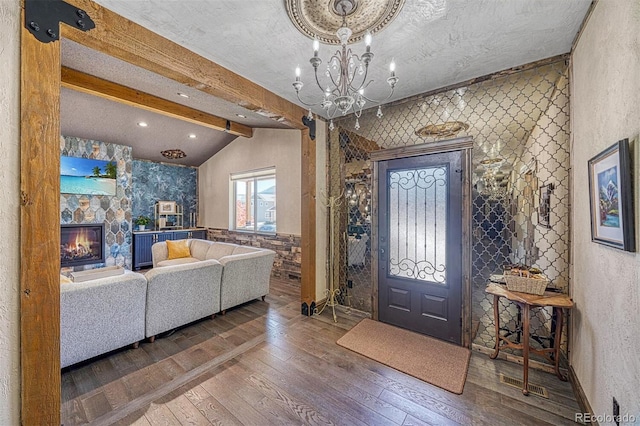 foyer with lofted ceiling with beams, a stone fireplace, wood-type flooring, and a chandelier