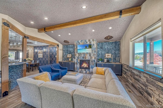 living room with lofted ceiling with beams, a fireplace, wood-type flooring, and a textured ceiling