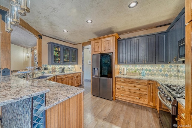 kitchen with light stone countertops, sink, stainless steel appliances, light hardwood / wood-style flooring, and kitchen peninsula