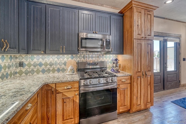 kitchen featuring light stone countertops, stainless steel appliances, light hardwood / wood-style flooring, and tasteful backsplash