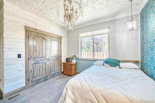 bedroom featuring wooden walls, ornamental molding, hardwood / wood-style flooring, and a notable chandelier