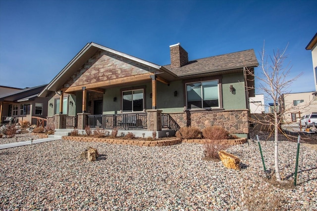 view of front of home featuring a shingled roof, stone siding, a chimney, a porch, and stucco siding