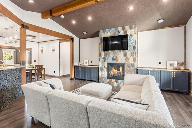 living area with dark wood-style flooring, lofted ceiling with beams, a textured ceiling, and a stone fireplace