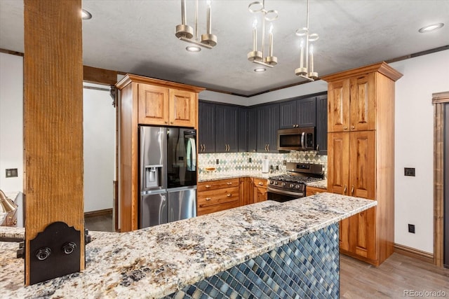 kitchen featuring light stone countertops, a peninsula, hanging light fixtures, appliances with stainless steel finishes, and decorative backsplash