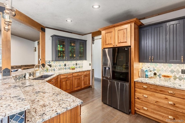 kitchen with brown cabinets, light stone countertops, a sink, wood finished floors, and stainless steel fridge