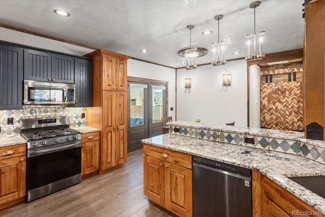 kitchen with hanging light fixtures, appliances with stainless steel finishes, decorative backsplash, light stone countertops, and brown cabinetry