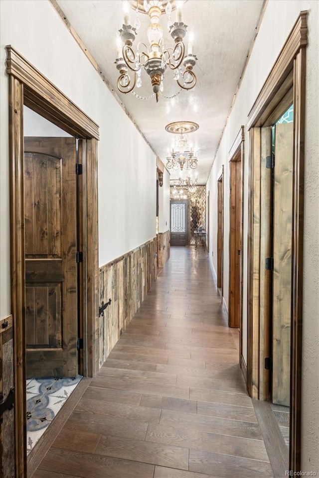 hallway with dark wood-style flooring, wainscoting, and an inviting chandelier