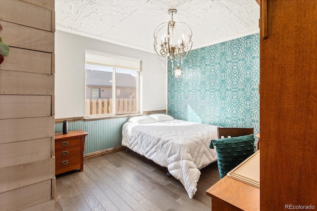 bedroom featuring crown molding, a notable chandelier, wainscoting, wood finished floors, and baseboards