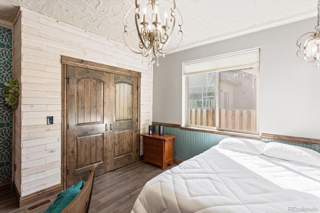 bedroom with a wainscoted wall, dark wood finished floors, visible vents, ornamental molding, and a chandelier