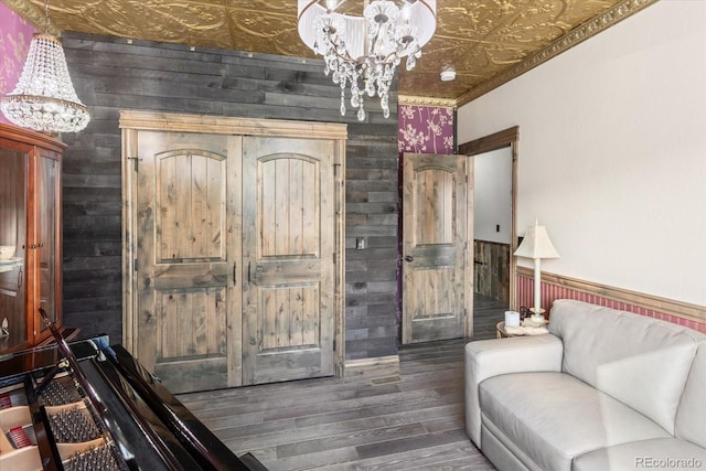 living room featuring wood walls, an ornate ceiling, a chandelier, and dark wood-style flooring