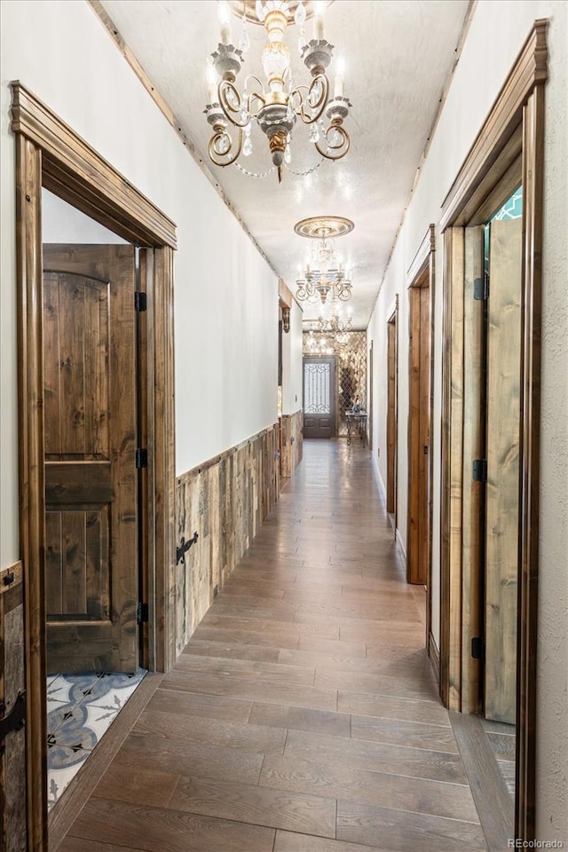 corridor with wood-type flooring, a chandelier, wainscoting, and a healthy amount of sunlight