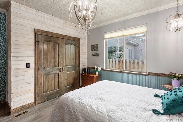 bedroom featuring wooden walls, a notable chandelier, wood finished floors, visible vents, and ornamental molding