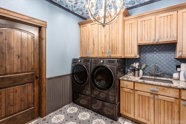 laundry area featuring washing machine and clothes dryer, cabinet space, a sink, a wainscoted wall, and a chandelier