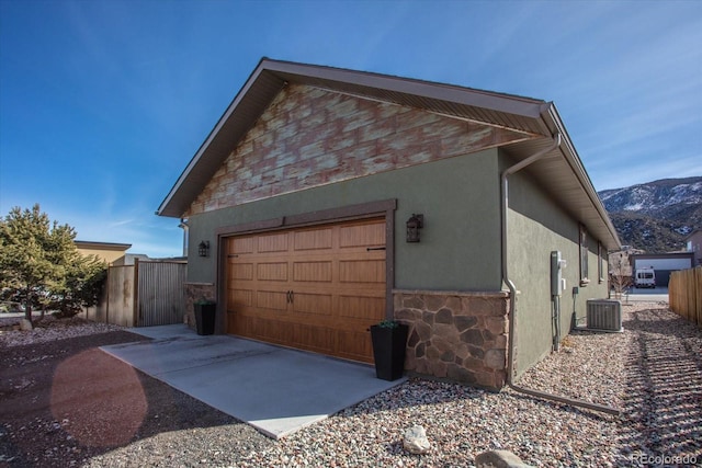 view of property exterior with central AC unit, stucco siding, stone siding, and fence