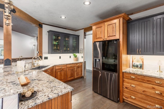 kitchen featuring a peninsula, glass insert cabinets, stainless steel refrigerator with ice dispenser, light stone counters, and a sink