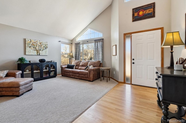 living area featuring light colored carpet, baseboards, high vaulted ceiling, and light wood-style flooring