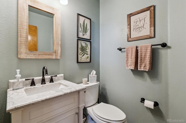 half bath featuring toilet, vanity, and a textured wall