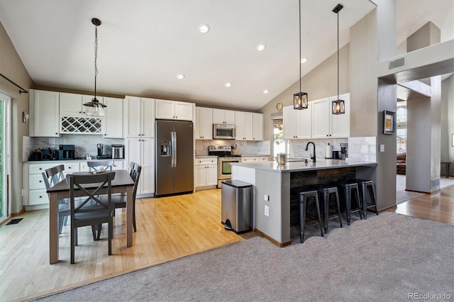 kitchen featuring decorative light fixtures, white cabinetry, stainless steel appliances, a peninsula, and a breakfast bar area