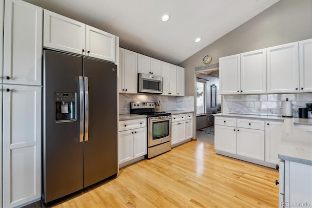 kitchen featuring light wood-style flooring, appliances with stainless steel finishes, white cabinets, and vaulted ceiling