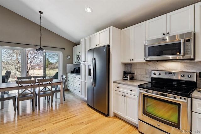 kitchen with tasteful backsplash, appliances with stainless steel finishes, white cabinets, light countertops, and lofted ceiling