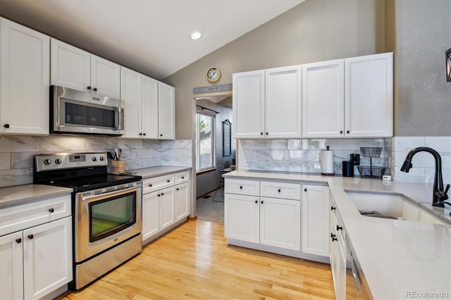 kitchen featuring light countertops, vaulted ceiling, appliances with stainless steel finishes, white cabinetry, and a sink