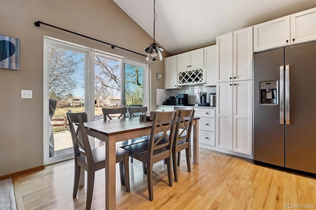 dining space featuring baseboards, lofted ceiling, and light wood finished floors