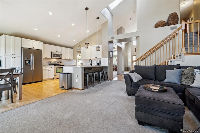 living room with high vaulted ceiling, light colored carpet, recessed lighting, and stairs