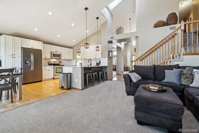 living room with light carpet, high vaulted ceiling, recessed lighting, stairway, and light wood finished floors