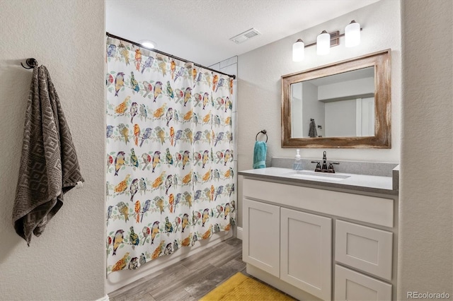 bathroom with vanity, wood finished floors, visible vents, curtained shower, and a textured wall