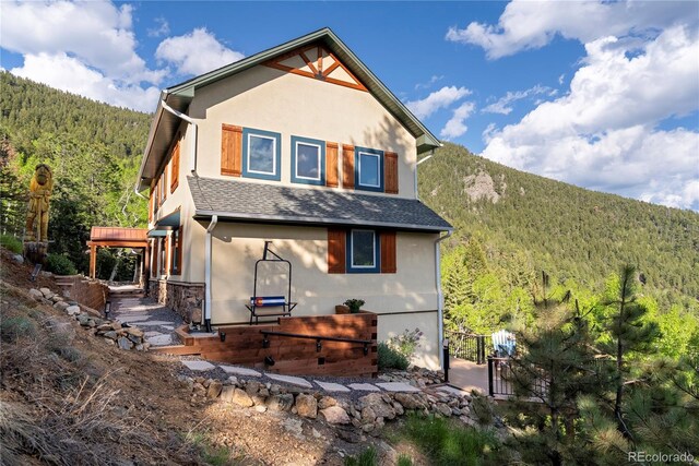 1194 Snyder Mountain Rd, Evergreen, CO 80439 - back of house featuring a forest view, stucco siding, a mountain view, and a shingled roof