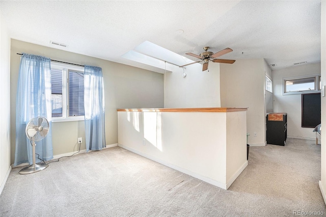 empty room with a skylight, visible vents, light carpet, a textured ceiling, and baseboards