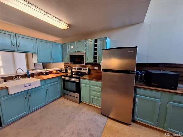 kitchen featuring blue cabinetry, appliances with stainless steel finishes, dark countertops, and a sink