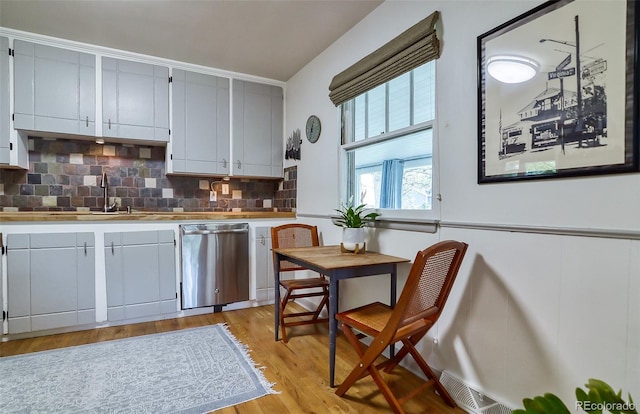 kitchen featuring stainless steel dishwasher, tasteful backsplash, light wood-style flooring, light countertops, and a sink