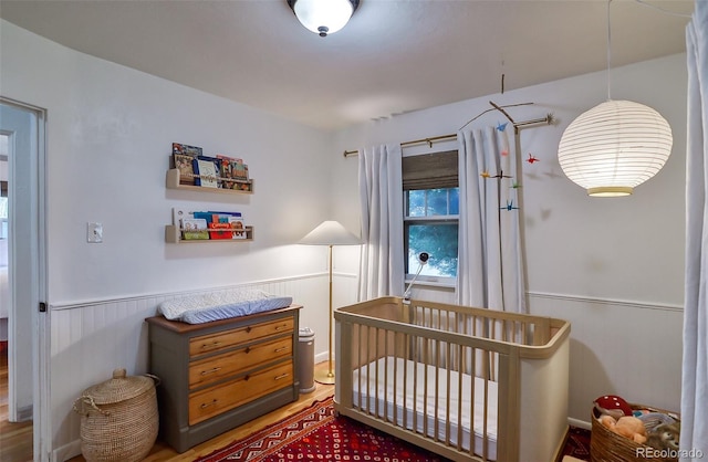 bedroom featuring wainscoting and a nursery area