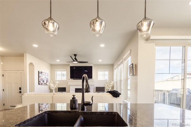 kitchen featuring a sink, dark stone countertops, open floor plan, and a ceiling fan