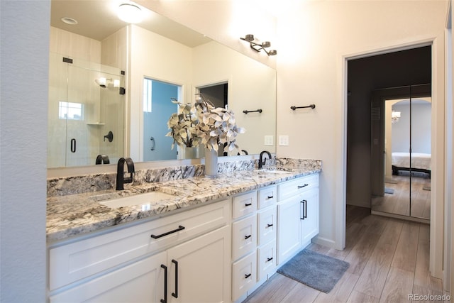 full bath featuring double vanity, a shower stall, wood finished floors, and a sink