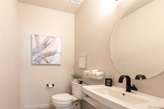 half bath featuring toilet, baseboards, visible vents, and a sink