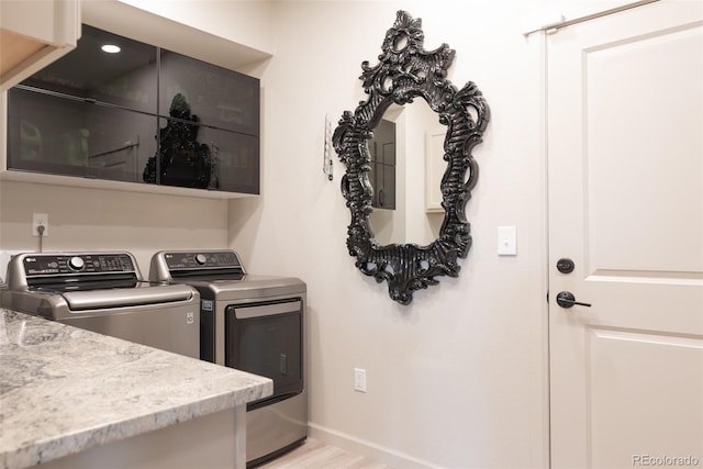 clothes washing area featuring light wood finished floors, laundry area, washing machine and dryer, and baseboards